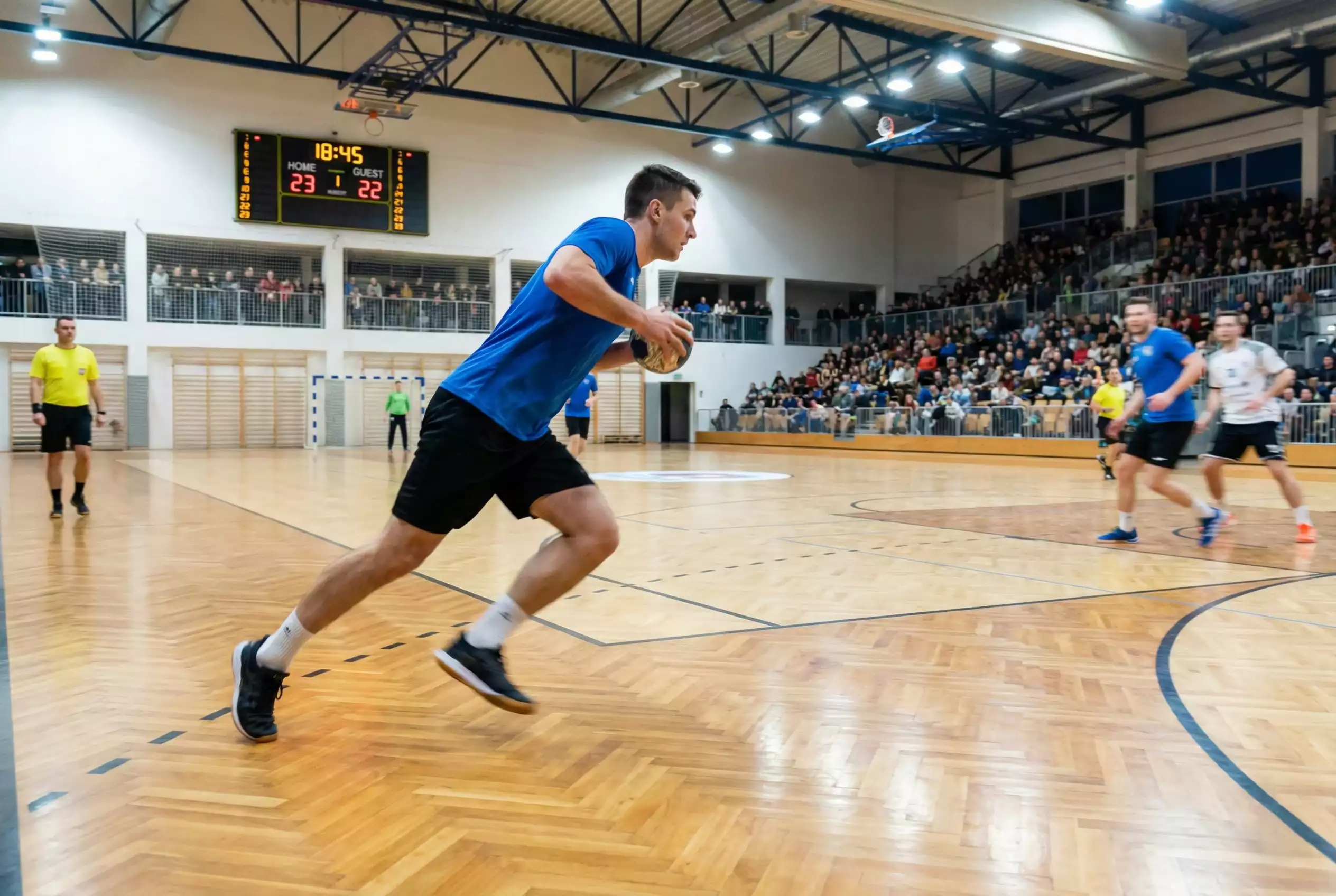 Action rapide lors d'un match de handball avec le tableau d'affichage visible en arrière-plan